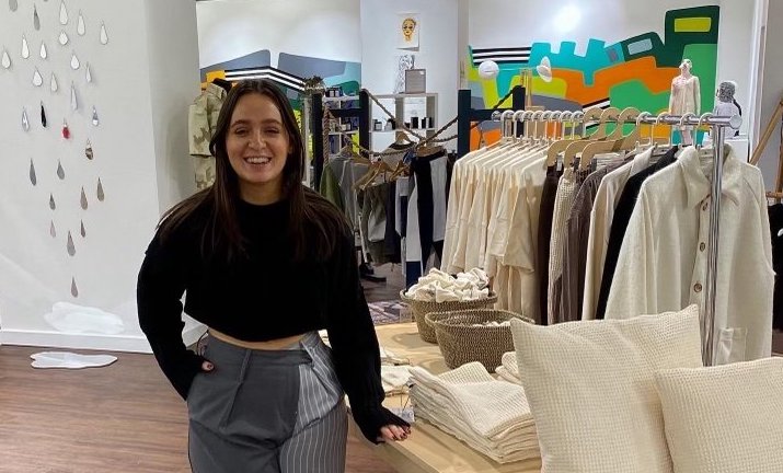 Amy Kohl in a clothes shop in black jumper and grey trousers
