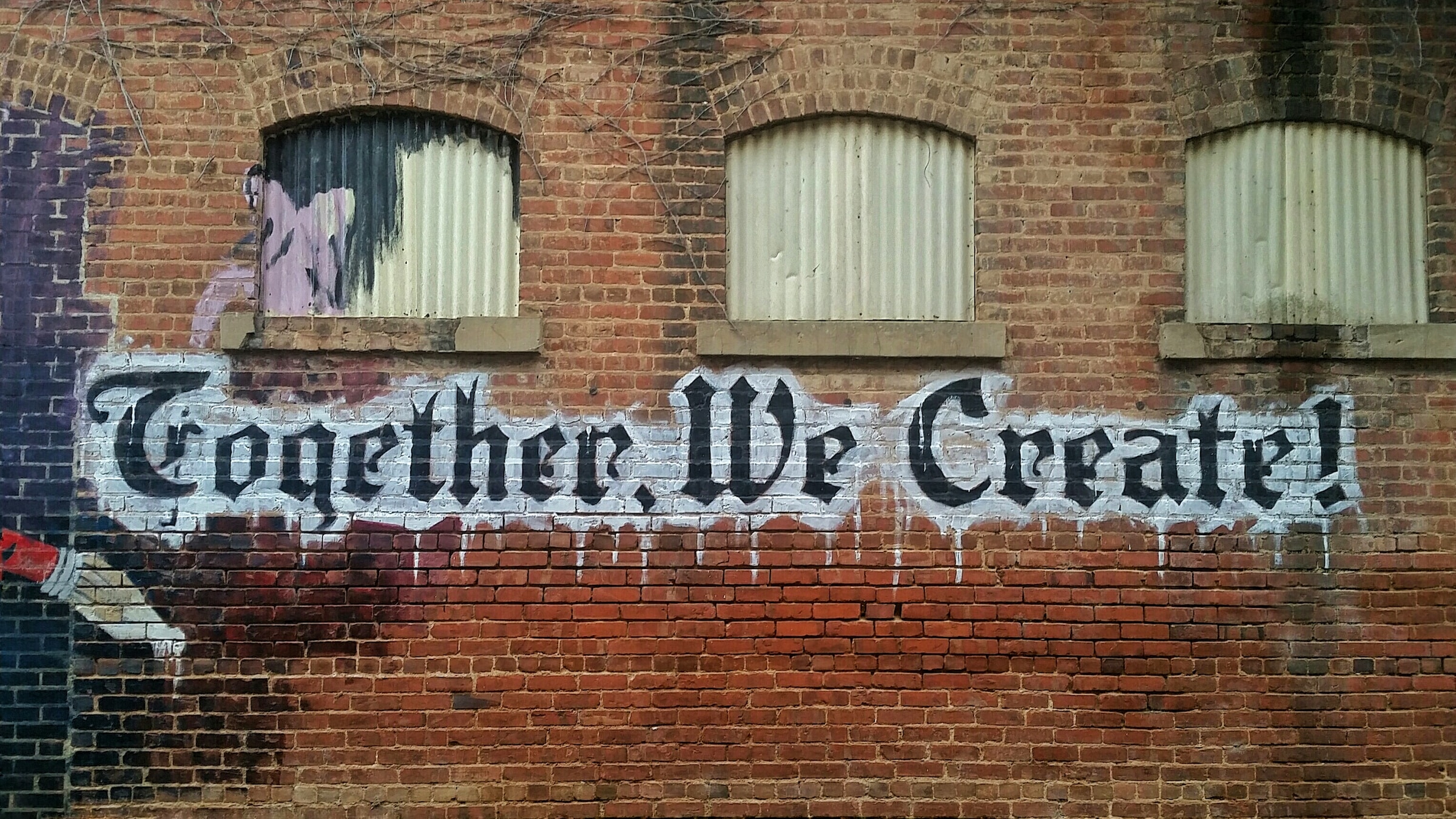 The words 'Together we create' in graffiti on a brick wall